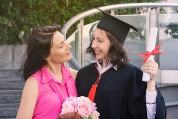 Young beautiful woman graduate and her mother at graduation ceremony, University Graduation...