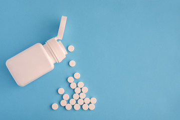 Container with white pills on light blue background. Pills spilling out of white bottle
