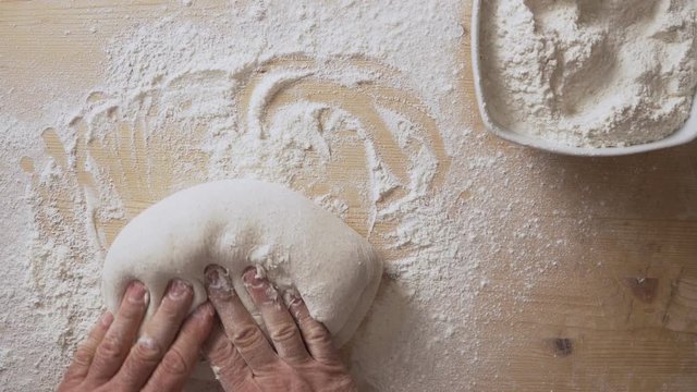 Slow motion top view of man's hands massaging pizza dough to prepare it for leavening at home on a light wooden board with white flour