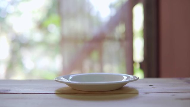 Footage B roll of hand placing hot ceramic white hot coffee cup on saucer over wooden table in nature green background. Breakfast and good food.