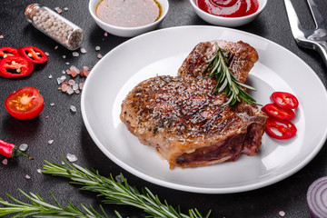 Fresh delicious juicy steak on the bones with vegetables and spices against a dark background