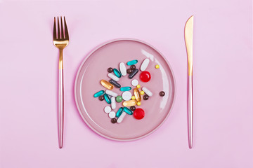 Colorful capsules and pills on plate with fork and knife on pink background. Diet, medicine, health concept