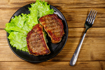 Grilled pork steaks with lettuce leaves on wooden table. Top view