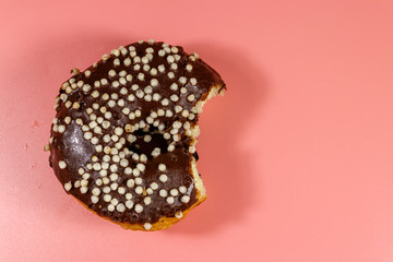 Bitten tasty chocolate donut on a pink background. Top view