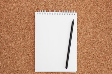 Black pencil on white notebook on cork background