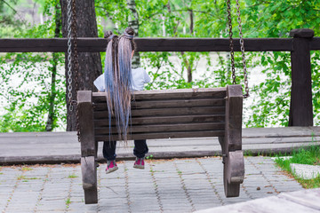 Beautiful girl with long dreadlocks on her head is resting on park bench.