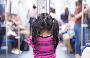 back of asian child or kid girl enjoy standing in bogey of sky train or electric train with underground railways or subway metro and holding rail for happy travel or transportation fun in city street