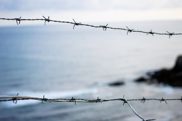 The silhouette of a barb wire fence in front of the sea