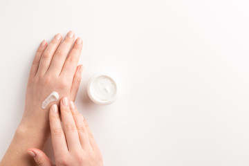 Care cosmetic concept. Woman applying cosmetic cream on hands, isolated on white background. Flat lay, top view, copy space.