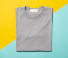 Grey folded t-shirt isolated on yellow and blue background.