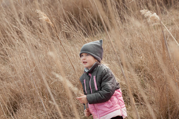 Cute little girl staying among reed at first sunny spring day and looking cheerfully, happy family weekend