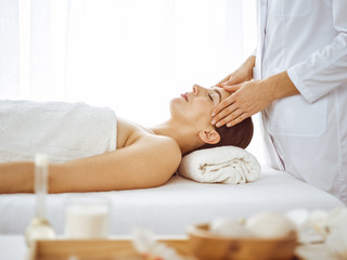 Fototapeta na wymiar Beautiful brunette woman enjoying facial massage with closed eyes. Relaxing treatment in medicine and spa center concepts