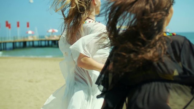 Two girls in bikini and pareo are running towards the sea on the beach.1.