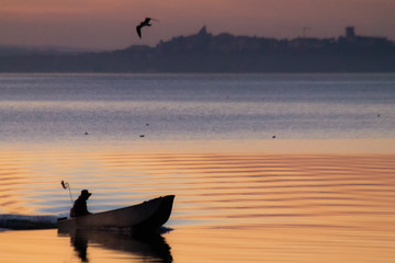 Trasimeno lake at sunset with a man on a little boat and birds