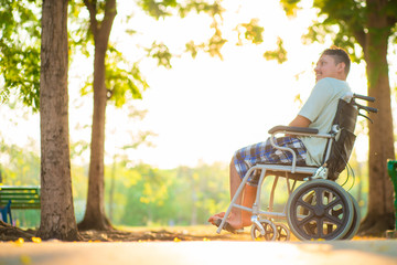 Young disabled asian man sitting on wheelchair in city park sunset light