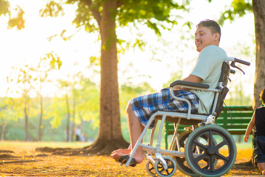 Young Disabled Asian Man Sitting On Wheelchair In City Park Sunset Light