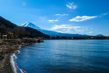 An idyllic view on Mt Fuji from the side of Kawaguchiko Lake, Japan. The mountain is surrounded by clouds. Soft reflections in calm surface of the lake. Serenity and calmness. Few ducks on the lake