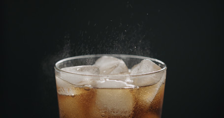 cola in glass with ice cubes on black background closeup