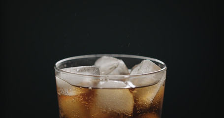cola in glass with ice cubes on black background closeup