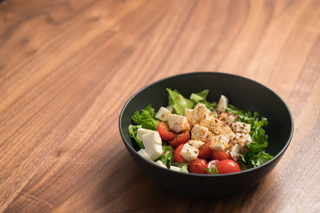 Healthy light salad with cherry tomatoes, mozzarella and frisee in black bowl on walnut surface