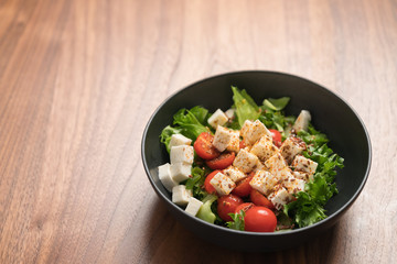 Healthy light salad with cherry tomatoes, mozzarella and frisee in black bowl on walnut surface