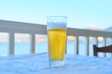 One glass of light beer on table in resort cafe, sea sunset background