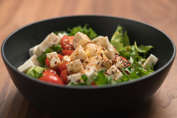 Healthy light salad with cherry tomatoes, mozzarella and frisee in black bowl on walnut surface closeup