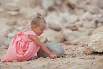 Small girl walks on the sea coast, she is wearing a coral dress, the kid travels along the sea