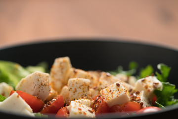 Healthy light salad with cherry tomatoes, mozzarella and frisee in black bowl on walnut surface closeup