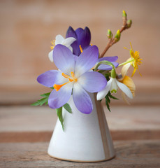 Mix of spring flowers: crocus, snowdrop and other field early flowers in a mini vase isolated on wooden background