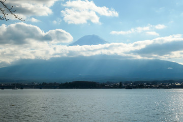 A close up view on Mt Fuji from the side of Kawaguchiko Lake, Japan. The mountain is hiding behind the clouds. Top of the volcano covered with a snow layer. Serenity and calmness. Calm lake's surface