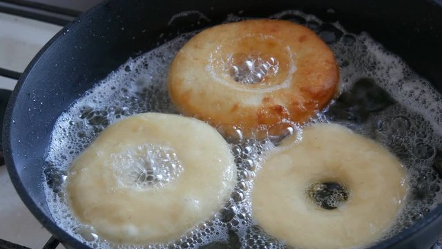 Delicious donuts frying in a pan. Large donuts are fried in hot oil in a pan. Homemade baking.