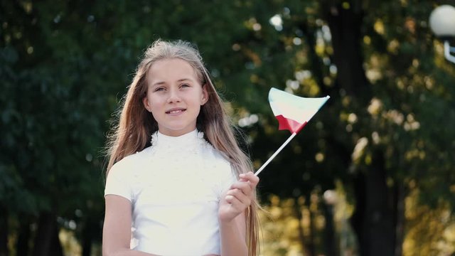 Blond girl closed eyes. Kid is in park holding Luxembourg flag. Background is green and blurred.