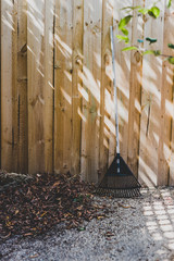 rake next to pile of fallen autumn leaves and wooden fence