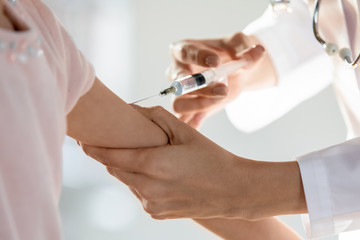 Close up female general practitioner making prick in arm of little patient. Small preschool girl...