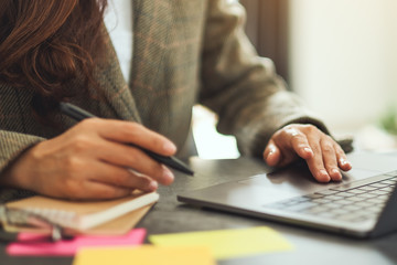 Businesswoman writing on paperwork while typing on laptop computer on the table in office