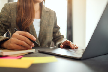 Fototapeta premium Businesswoman writing on paperwork while typing on laptop computer on the table in office