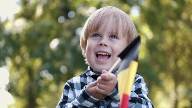 Kid holds flag of Belgium. He is playing with flag in park. The child is full of emotions.