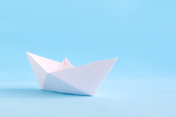 White paper handmade origami boat on the blue background. Sea summer travel theme.