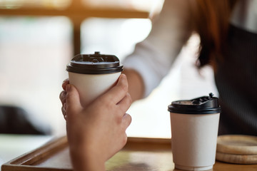 A waitress holding and serving paper cups of hot coffee to customer in cafe