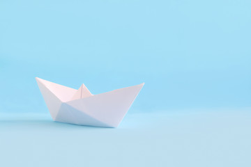 White paper handmade origami boat on the blue background. Copy space for your text. Theme of homemade toys for children.