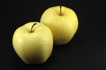 Two yellow apples on black background