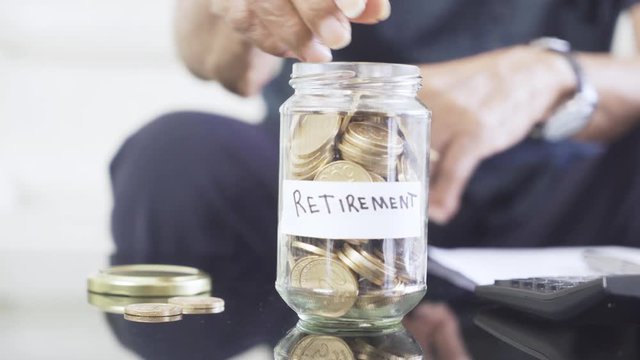 Elderly man hand saving golden coins into glass jar