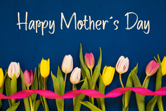 English Text Happy Mothers Day. White And Pink Tulip Spring Flowers With Ribbon. Blue Wooden Background