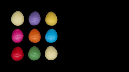 Fototapeta na wymiar Bright colourful candy Easter eggs arranged on a plain black background with copy space