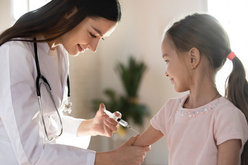 Side view pleasant young nurse injecting antibodies to fight viruses to little smiling girl....