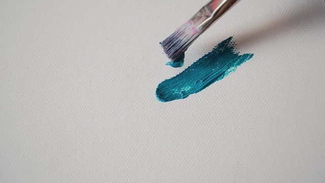 Art creation process closeup with brush fluently making blue oil brushtroke on white canvas.