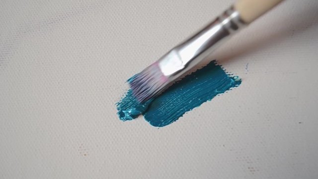 Art creation process closeup with brush and paint knife fluently making blue and yellow oil brushtrokes on white canvas.