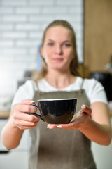 A young barista girl offers a large cup with coffee. Small business concept.