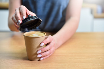 Barista making coffee and closes the paper cup with a lid, hands closeup. Coffee shop small business concept.